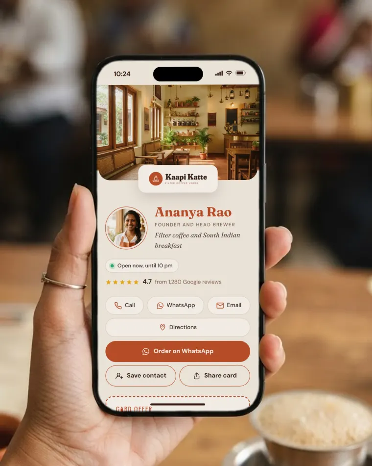 Phone in a café showing the Kaapi Katte web card: the café logo, the founder’s photo, call, WhatsApp, email and directions buttons, and Save contact